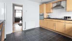 A modern kitchen with light wooden cabinets, a stainless steel range hood, and a black tiled floor. - Traditional Belfast Home, Walking Distance to City & Titanic Heritage (Belfast)