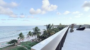 Vista al mar desde un balcón, con palmeras, una playa arenosa y cielo despejado.