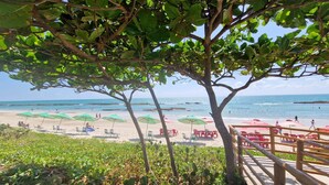 Ein Strand mit Sonnenschirmen und Liegen, eine Holzterrasse und Blick auf den Ozean.