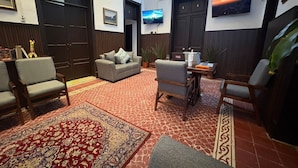 Een ruime woonkamer met een bank, fauteuils, een salontafel en een aan de muur bevestigde televisie.