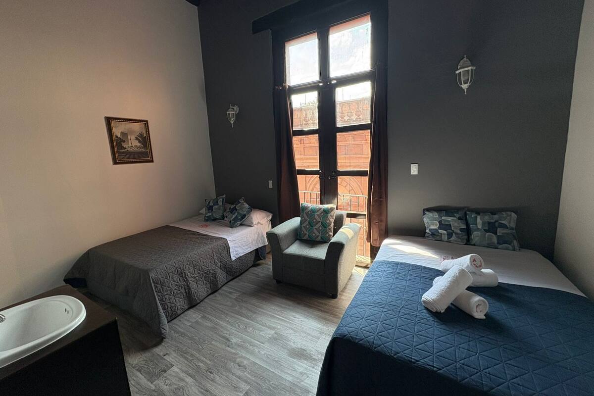 Une chambre avec deux lits simples, un petit canapé, une fenêtre avec des rideaux et un tableau au mur.