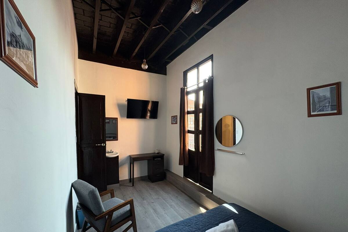 Une chambre à coucher comprenant un lit, une chaise, un bureau, une télévision, un miroir et une porte donnant sur une vue agréable.