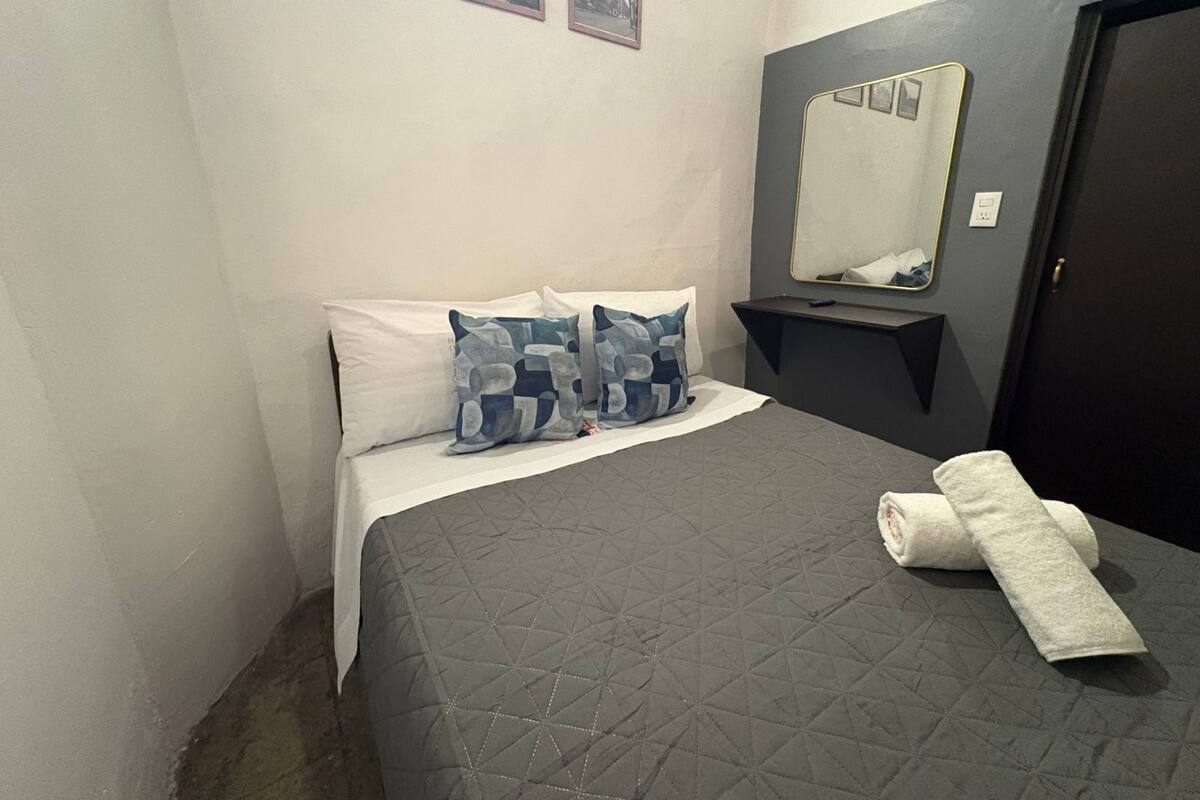 Une chambre à coucher avec un lit, des oreillers, une serviette, un miroir et un mur orné de trois tableaux.