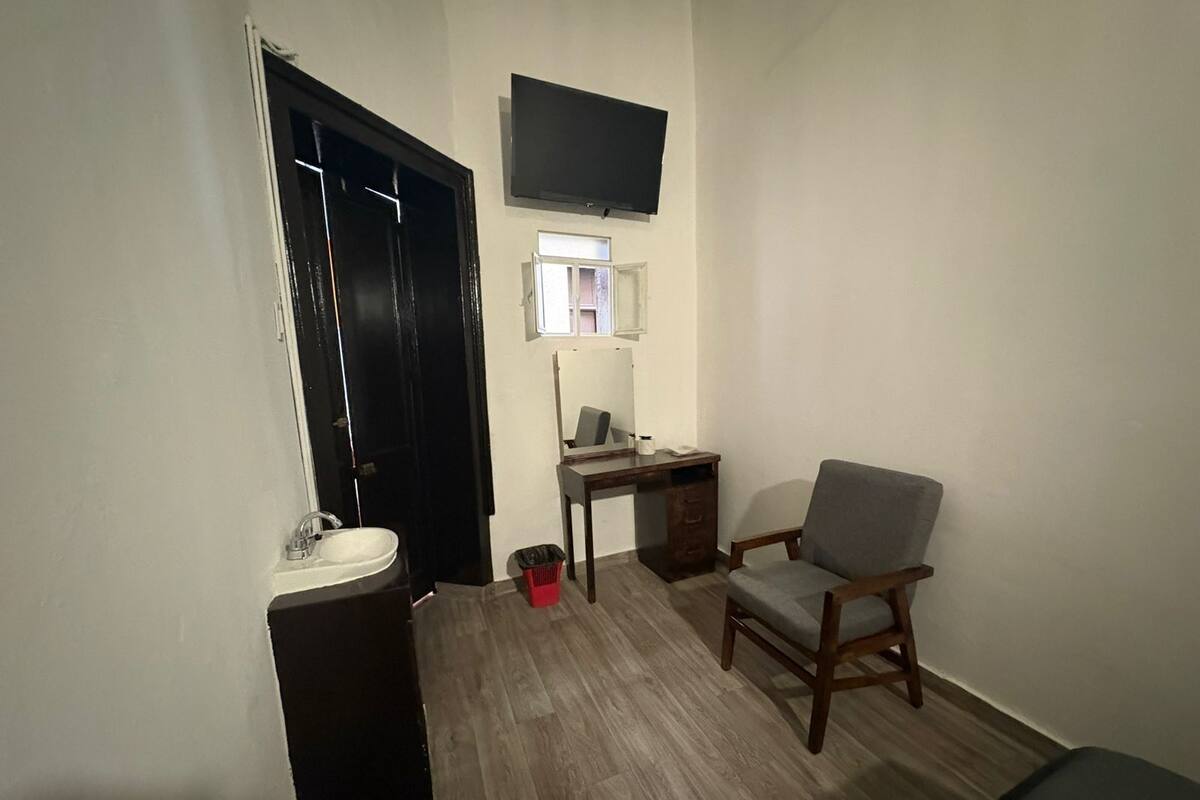 Une petite pièce avec un bureau, une chaise, un téléviseur et une fenêtre.