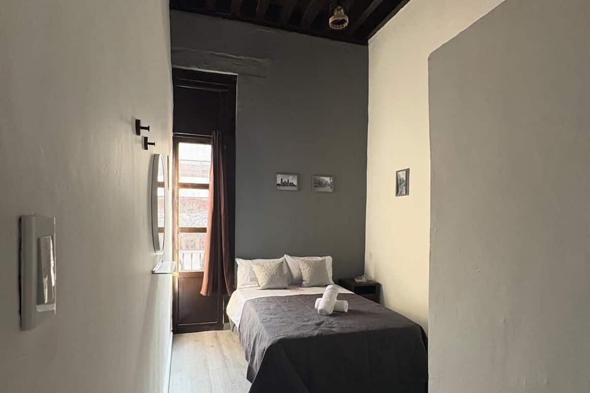 Un couloir étroit mène à une chambre à coucher qui contient un lit, une table de chevet et une fenêtre.
