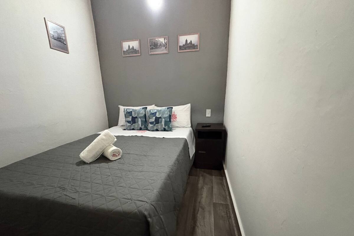 Une petite chambre à coucher, bien rangée, avec un lit, des oreillers, une table de chevet et une commode.