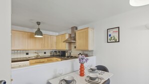 A modern kitchen with wooden cabinets, a stainless steel range hood, and a dining area with a table set for two. - Stylish 1-Bed Flat in London’s Prime Diamond District (London)