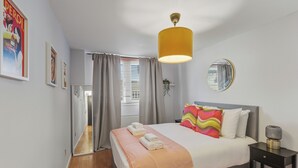 A hotel room with a bed, a bedside table, a mirror, and a window with curtains. - Stylish 1-Bed Flat in London’s Prime Diamond District (London)