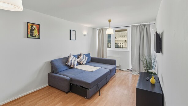 A modern living room with a sofa, a small table, a vase with flowers, and a picture on the wall. - Stylish 1-Bed Flat in London’s Prime Diamond District (London)