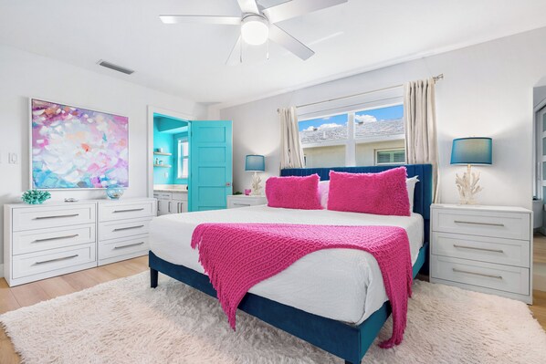 A bedroom with a bed, white drawers, a ceiling fan, a window with curtains, and a painting on the wall. - Colorful villa w/ 2 king beds, heated pools & beach access (Siesta Key)