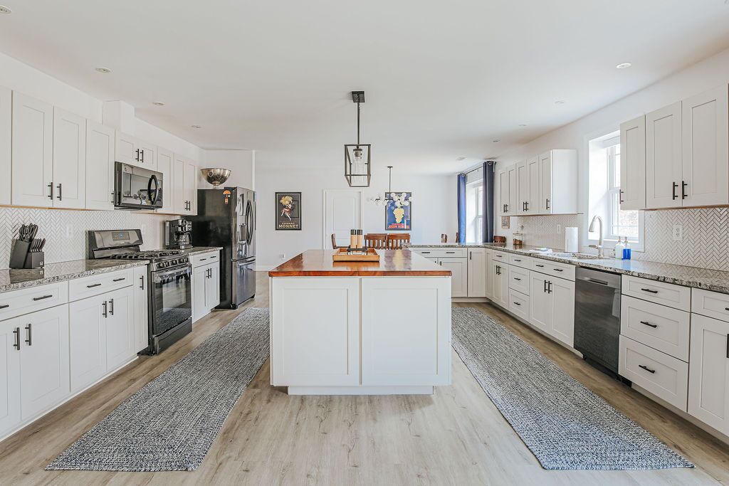 Et moderne køkken med hvide skabe, en central ø, rustfrie stålensapparater og et backsplash i fiskebensmønster.