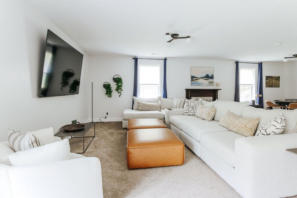 A modern living room with a white sofa, a brown ottoman, a flat-screen TV, and a fireplace.