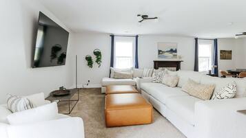 A modern living room with a white sofa, a brown ottoman, a flat-screen TV, and a fireplace.