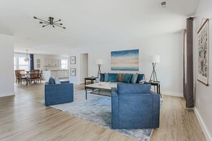 Een ruime woonkamer met een blauwe zithoek, een salontafel en een schilderij aan de muur.