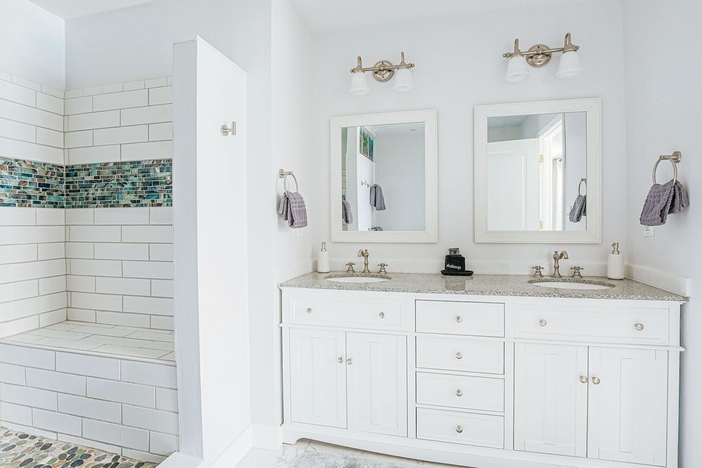 A bathroom with white cabinets, two sinks, and a shower area with mosaic tiles.