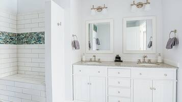 A bathroom with white cabinets, two sinks, and a shower area with mosaic tiles.