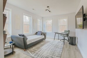 Ein modernes Schlafzimmer mit Bett, Schreibtisch und Stuhl. Große Fenster und eine Deckenleuchte sind vorhanden.