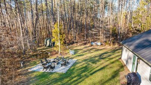 Un jardin avec un foyer, des chaises de jardin et un espace barbecue abrité.