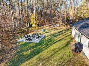 A backyard with a fire pit, lawn chairs, and a covered grill area.