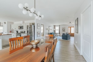 A modern kitchen with white cabinets, a wooden dining table, and a chandelier.
