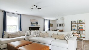 Una sala de estar con un sofá seccional, otomanas, una chimenea y una estantería.