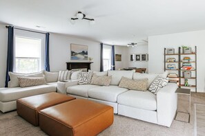 Ein Wohnzimmer mit Ecksofa, Poufs, Kamin und Bücherregal.