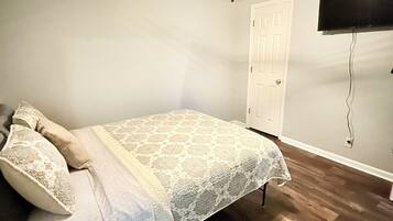 A bedroom with a bed, a ceiling fan, a TV mounted on the wall, and a door.
