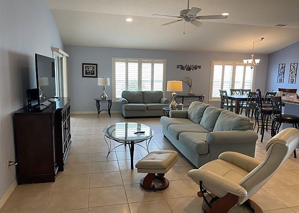 A spacious living room with a sofa, armchair, and coffee table, a dining area with chairs, and a television on a cabinet.