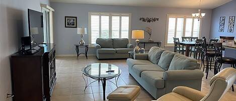 A spacious living room with a sofa, armchair, and coffee table, a dining area with chairs, and a television on a cabinet.