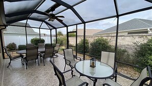 Une terrasse couverte avec une table et des chaises, un ventilateur de plafond et une vue sur un quartier résidentiel.