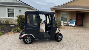 Une voiturette de golf noire et compacte est garée devant un immeuble d’habitation dont la façade est en pierre et l’extérieur de couleur beige.