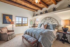 A bedroom with a large bed, a chair, a bench, and a window with a view. - Santa Fe Hacienda Style Estate | Courtyard and Fireplaces (Santa Fe)