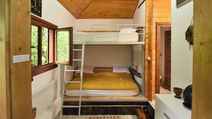 Ein kompakter Raum mit Etagenbett, Fenster mit Blick auf Grünflächen, Holzboden und einem kleinen Regal mit einem dekorativen Gegenstand.