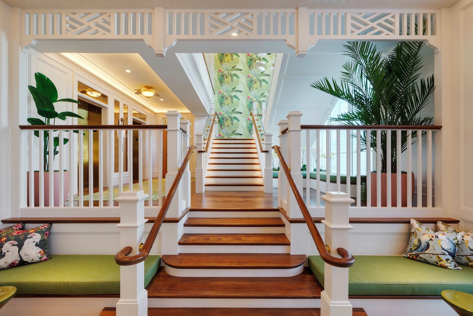 Una escalera con escalones de madera y barandillas blancas que conduce a una habitación con un sofá verde y una pared decorada con un mural tropical.