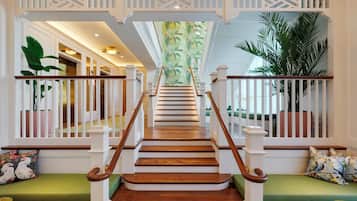 Una escalera con escalones de madera y barandillas blancas que conduce a una habitación con un sofá verde y una pared decorada con un mural tropical.