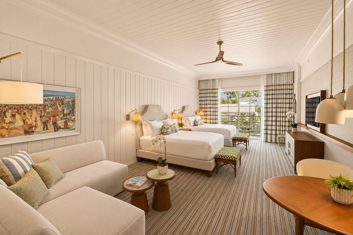 Quarto de hotel com cama, sofá, mesa de jantar e televisão.