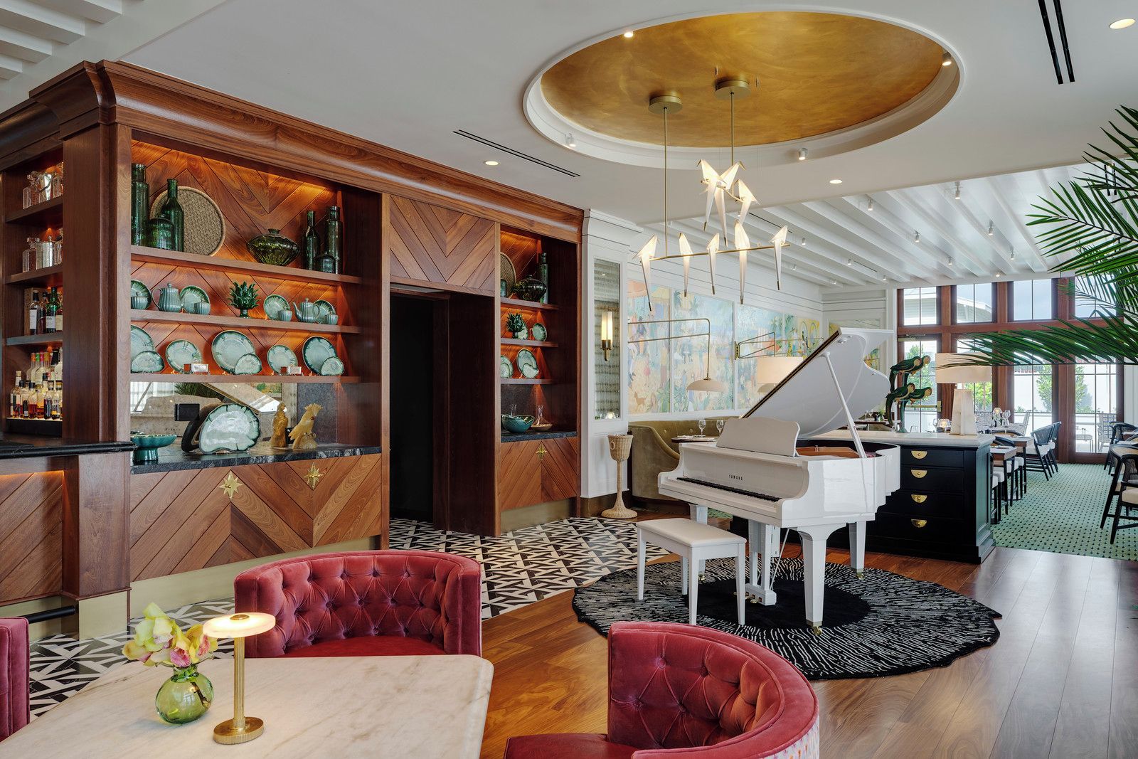 A spacious room with a grand piano, a wooden bar area, and a large window providing natural light.