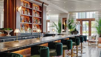 A bar area with a long counter, green upholstered bar stools, and shelves with bottles.