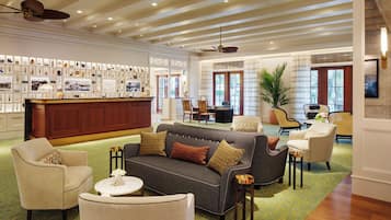 Een hotel lobby met een receptiebalie, een zithoek en een wand met ingekaderde objecten.