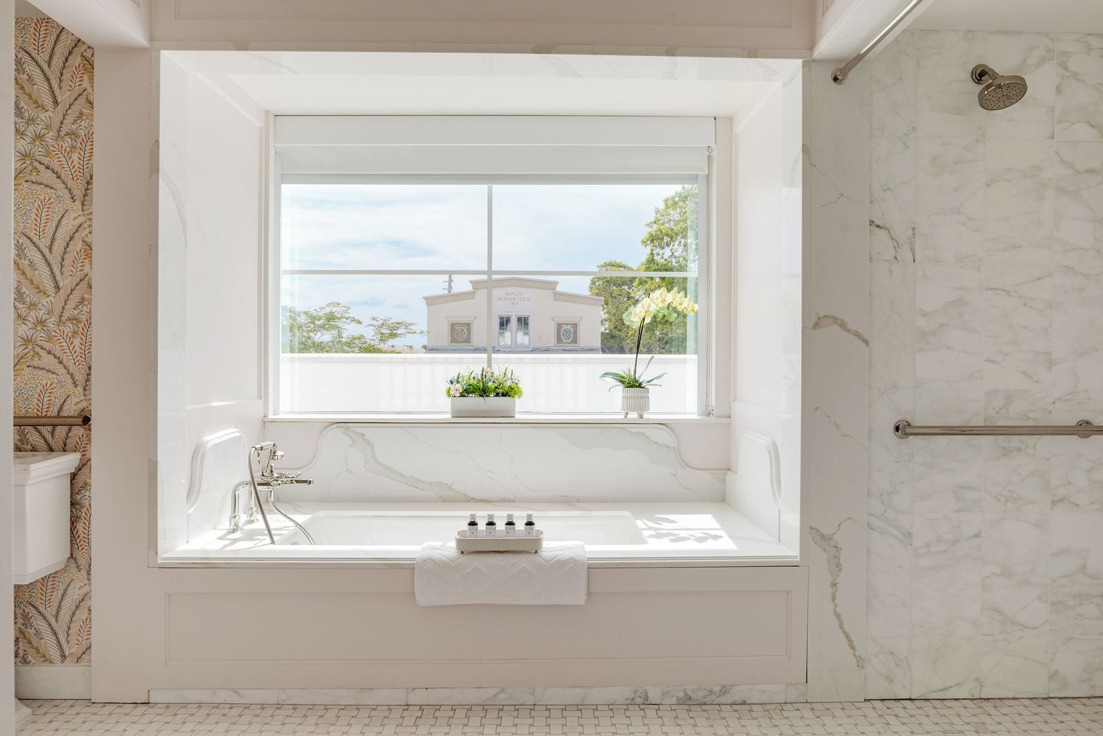 A bathroom with a bathtub, a window with a view of a building, and a shower area.