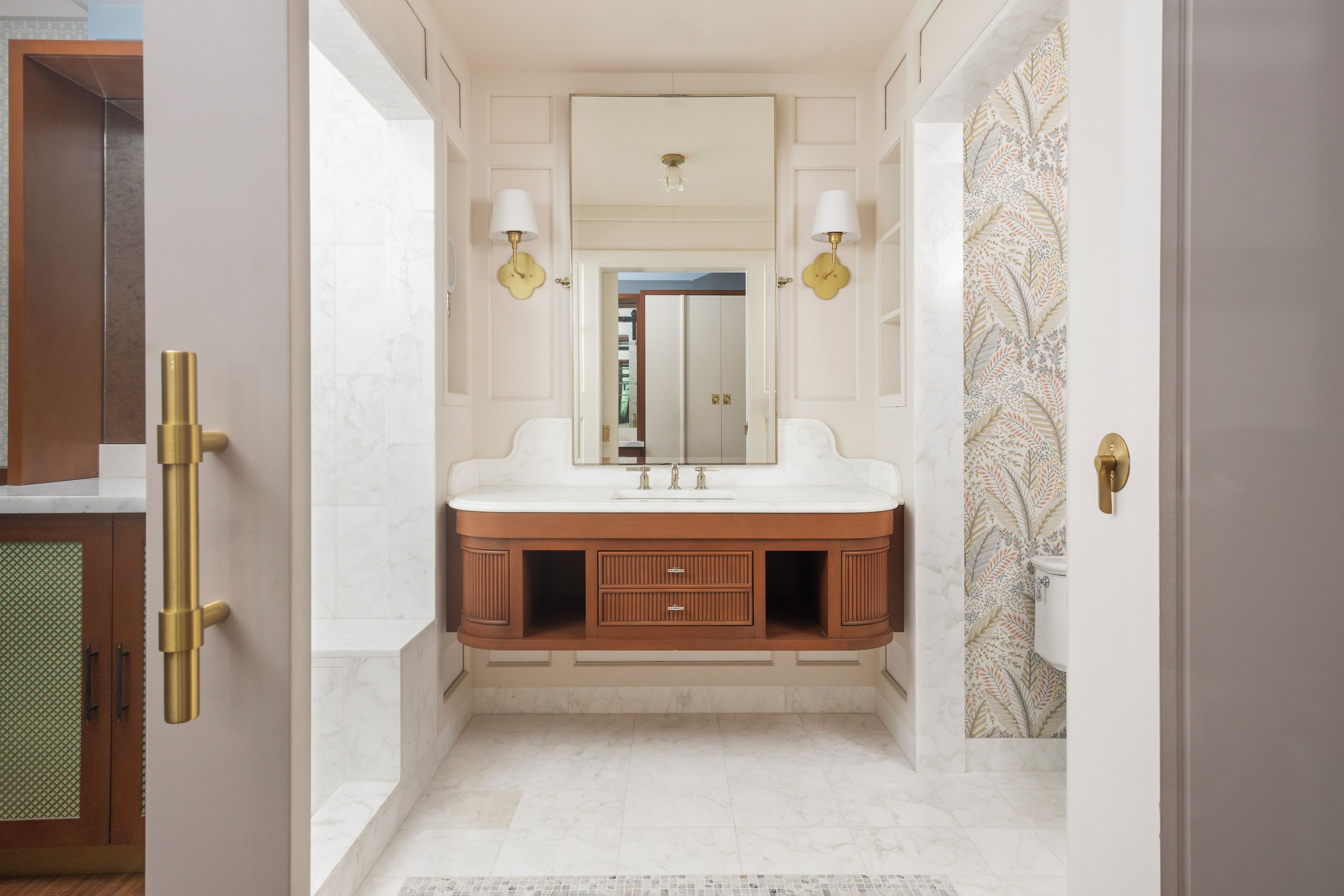 A bathroom with a marble vanity, two wall-mounted lights, a mirror, and a patterned wallpaper.