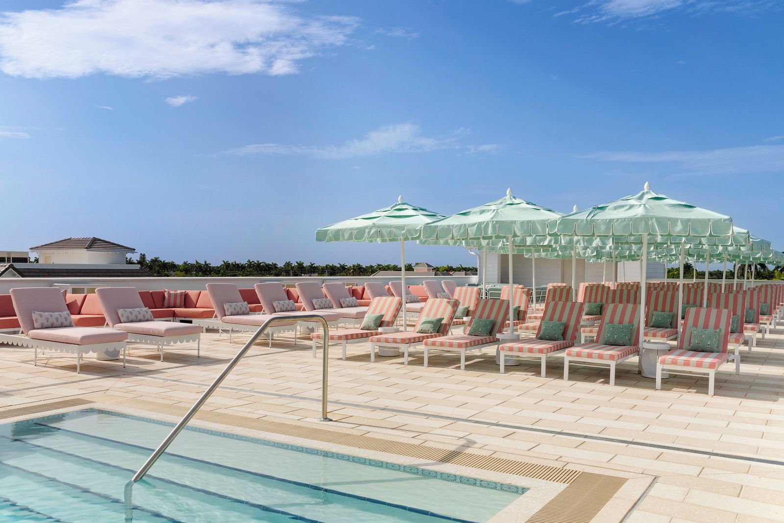 A poolside area with lounge chairs and umbrellas, a clear sky, and a building in the background.