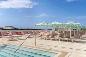 Un espace aménagé au bord de la piscine, avec des chaises longues et des parasols, un ciel dégagé et un bâtiment en arrière-plan.
