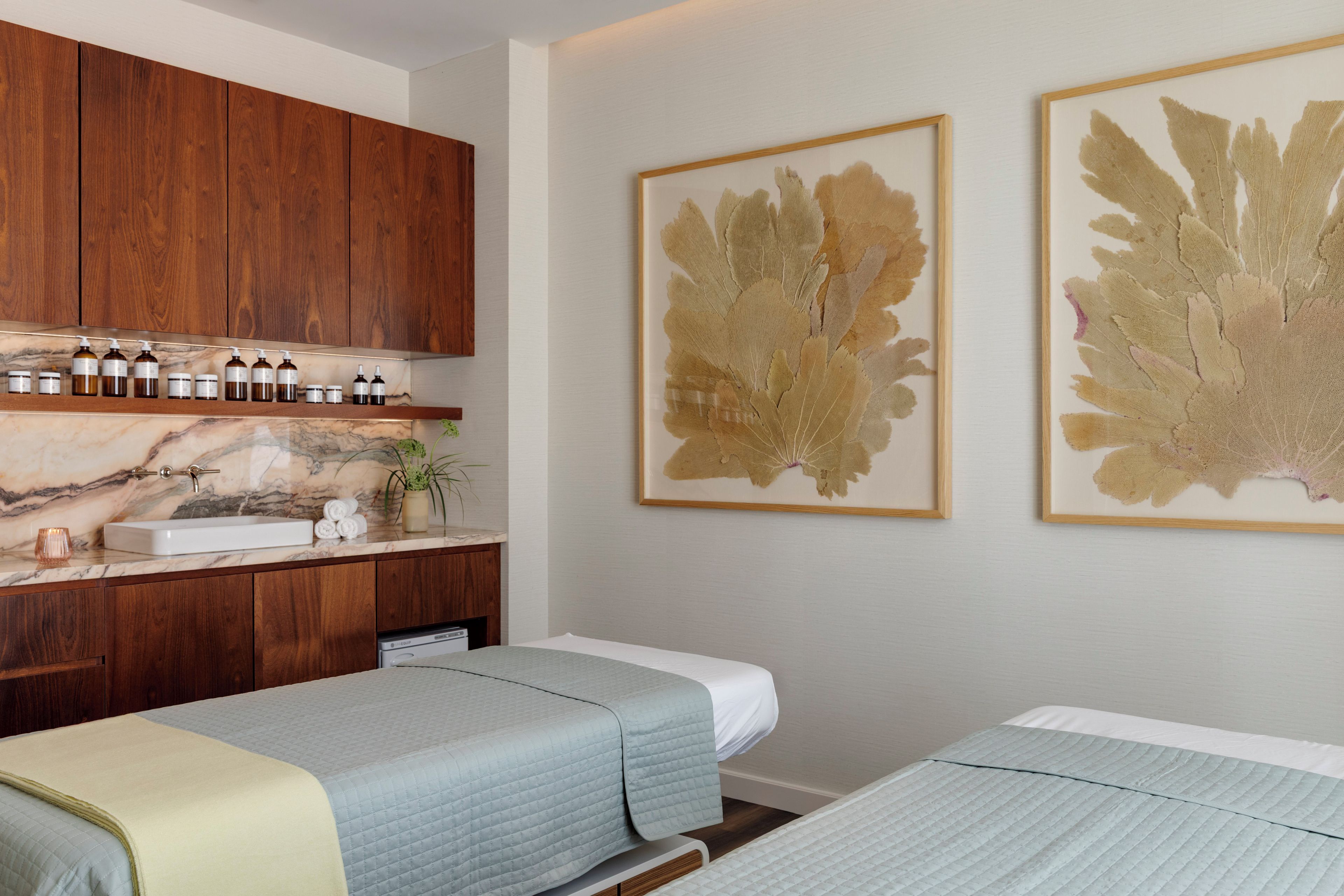A hotel room with a wooden cabinet, a marble countertop, a sink, and two beds with light blue bedding.