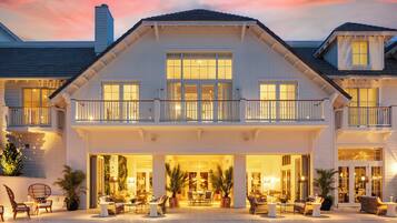 Una casa grande de varios pisos con un balcón, ventanas amplias y un área de estar exterior con muebles.