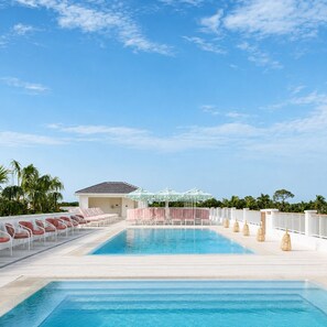 A swimming pool with lounge chairs and umbrellas, surrounded by palm trees and a clear sky. - Olde Naples Hotel (Naples)