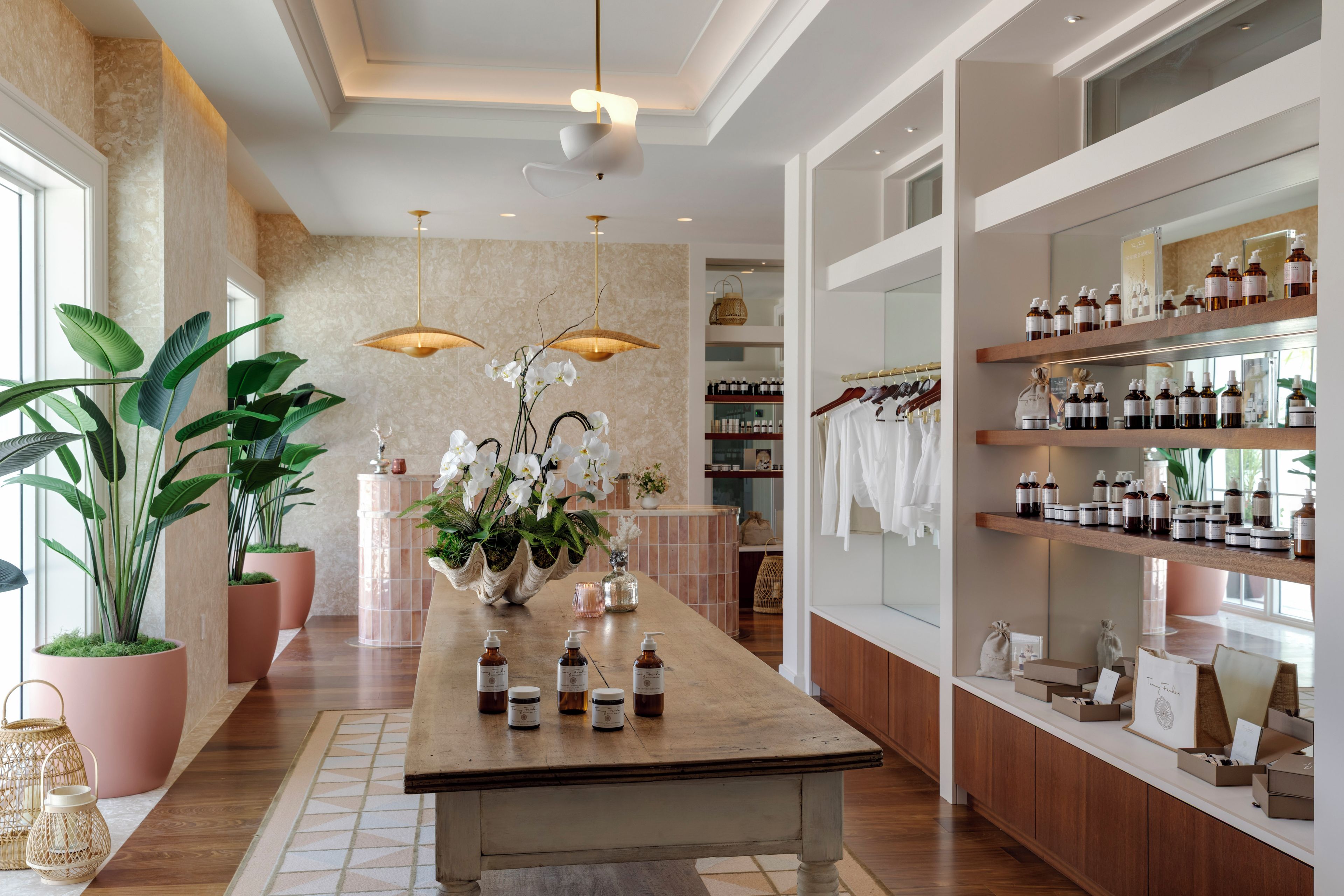 A well-lit, spacious room with a central island, potted plants, and shelves stocked with products.