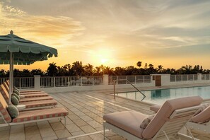 A poolside area with lounge chairs and a pool, surrounded by a white fence and palm trees, during sunset. - Olde Naples Hotel (Naples)