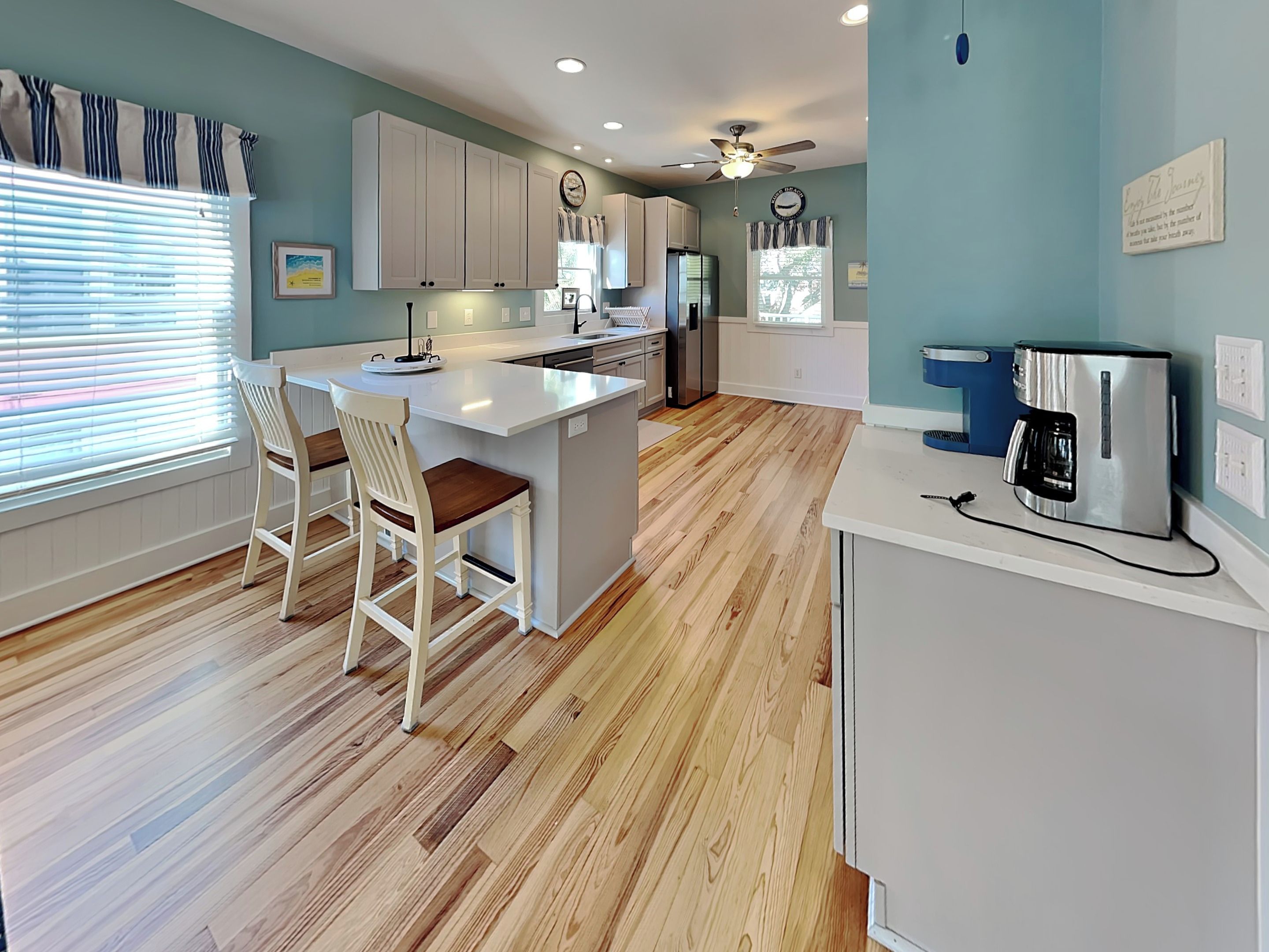 A modern kitchen with wooden flooring, white cabinetry, a central island, and a coffee maker.