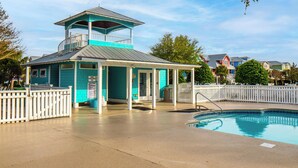 A turquoise lifeguard tower with a balcony, a covered seating area, and a pool. - In Sea State Escape (Kure Beach)